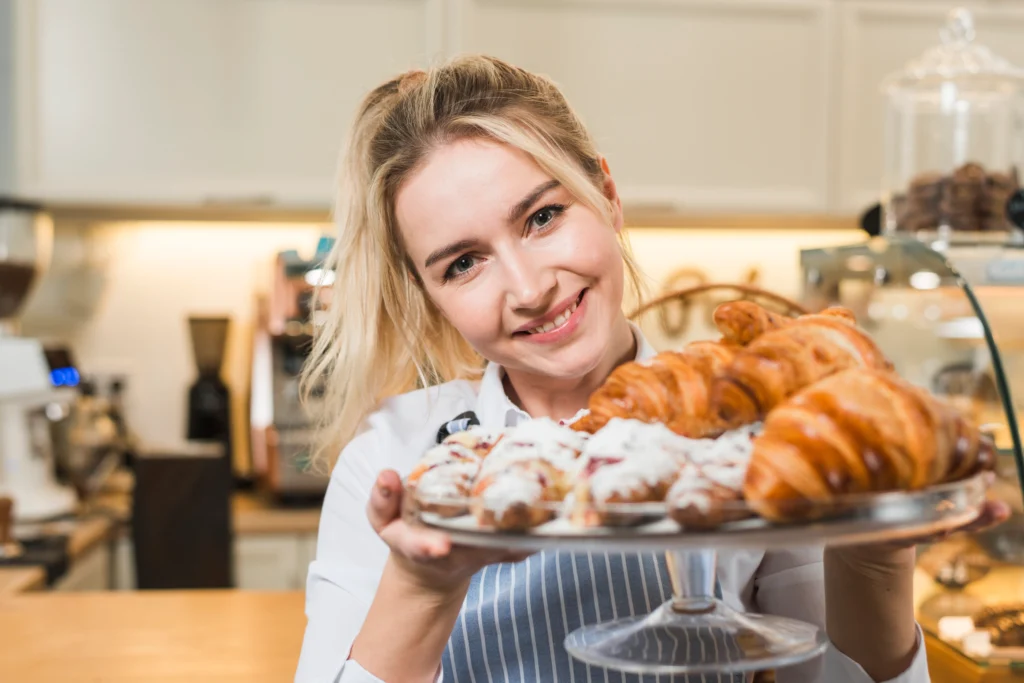 About Us 1 portrait smiling young woman holding baked croissant cake stand